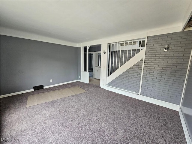 spare room featuring carpet floors and brick wall