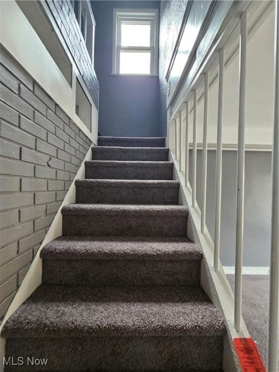 stairway featuring carpet flooring and brick wall