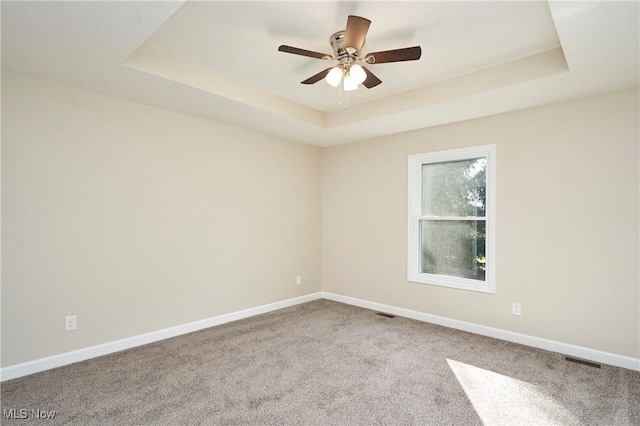 empty room featuring ceiling fan, a raised ceiling, and carpet floors