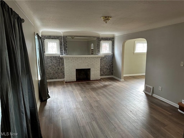 unfurnished living room featuring wood-type flooring, a textured ceiling, and a brick fireplace