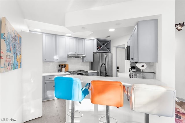 kitchen featuring stainless steel refrigerator, kitchen peninsula, stove, gray cabinets, and a breakfast bar