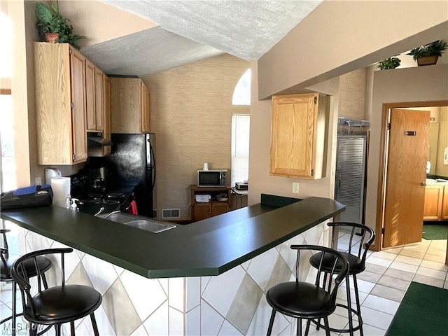 kitchen featuring sink, a kitchen breakfast bar, kitchen peninsula, a textured ceiling, and light tile patterned floors