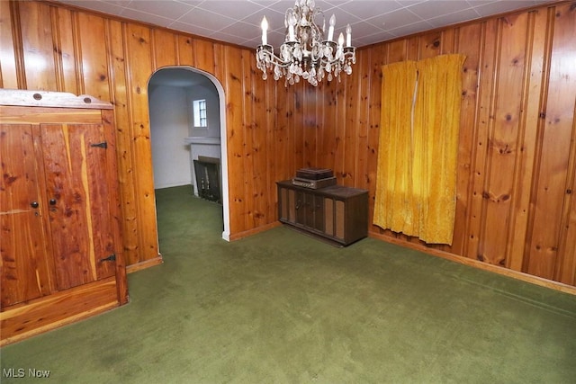 unfurnished dining area featuring dark carpet, an inviting chandelier, and wood walls