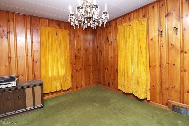 spare room featuring dark carpet, wooden walls, and a chandelier