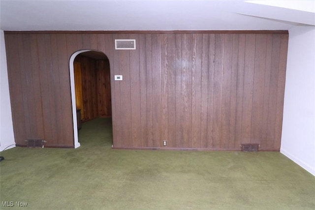 carpeted empty room featuring wood walls