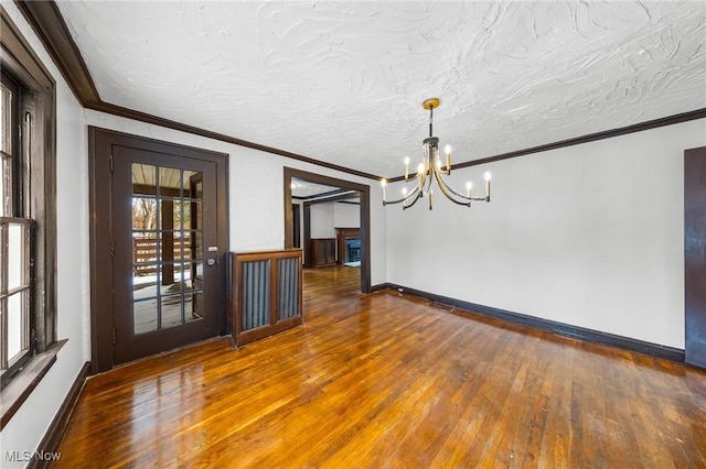 unfurnished dining area featuring ornamental molding, a textured ceiling, hardwood / wood-style flooring, and a notable chandelier