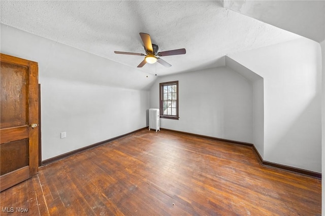 additional living space with a textured ceiling, radiator, dark wood-type flooring, and lofted ceiling