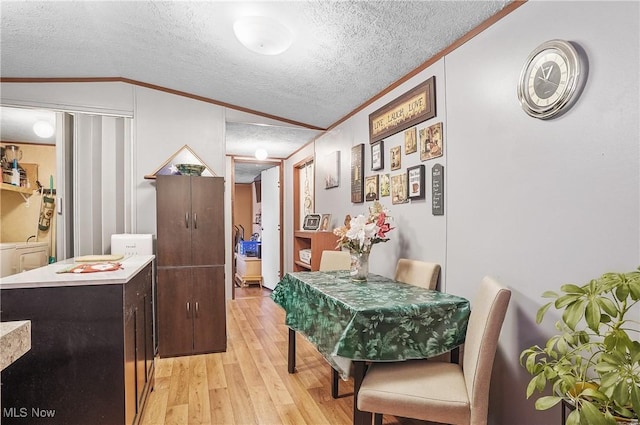 dining area featuring ornamental molding, a textured ceiling, vaulted ceiling, washer / clothes dryer, and light hardwood / wood-style floors