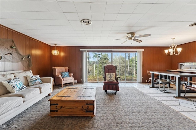 tiled living room with ceiling fan with notable chandelier and wooden walls