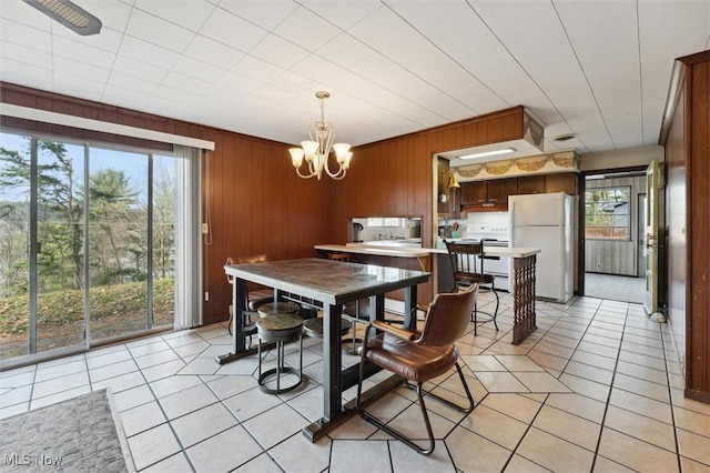 dining space featuring ceiling fan with notable chandelier, light tile patterned floors, and wooden walls