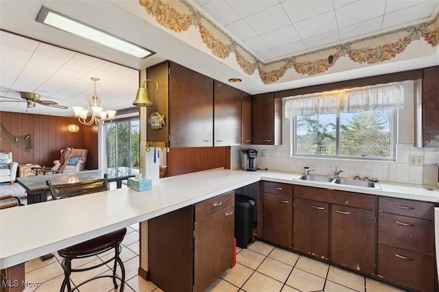 kitchen with sink, kitchen peninsula, pendant lighting, a breakfast bar, and ceiling fan with notable chandelier