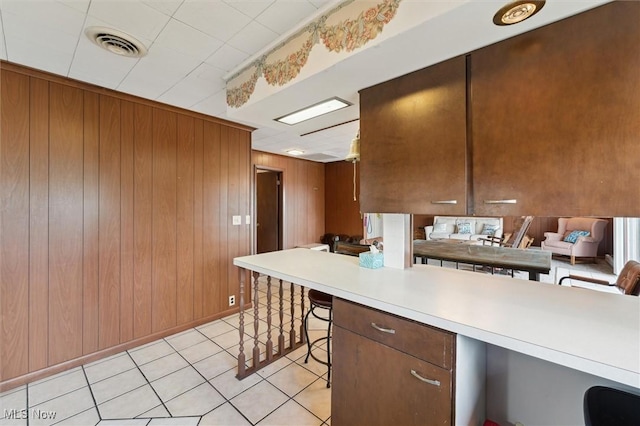 kitchen with a kitchen breakfast bar, kitchen peninsula, wooden walls, and light tile patterned floors