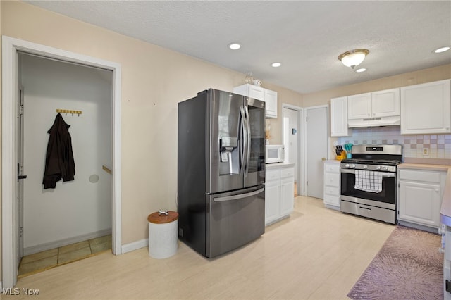 kitchen with backsplash, light wood-type flooring, a textured ceiling, white cabinetry, and stainless steel appliances