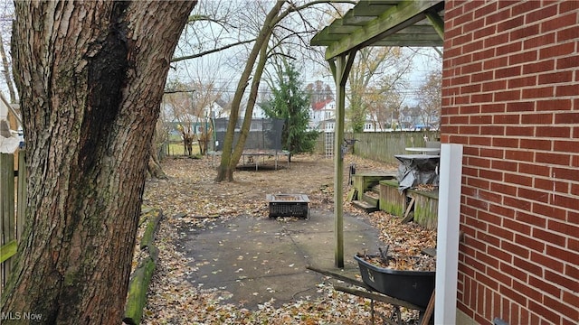 view of yard featuring a trampoline, an outdoor fire pit, and a patio area