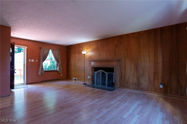 unfurnished living room featuring wood walls, light hardwood / wood-style floors, and a textured ceiling