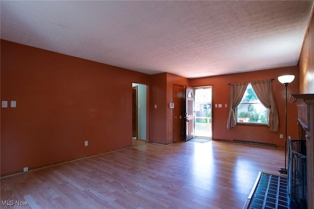 unfurnished living room with a textured ceiling, light hardwood / wood-style flooring, a baseboard heating unit, and a tiled fireplace