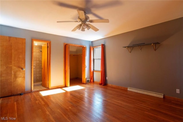 unfurnished bedroom with a baseboard heating unit, ceiling fan, a spacious closet, connected bathroom, and wood-type flooring