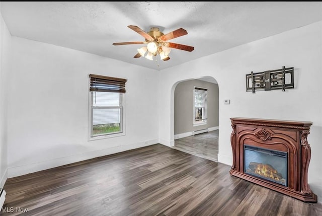 unfurnished living room featuring a textured ceiling, dark hardwood / wood-style flooring, a baseboard radiator, and ceiling fan