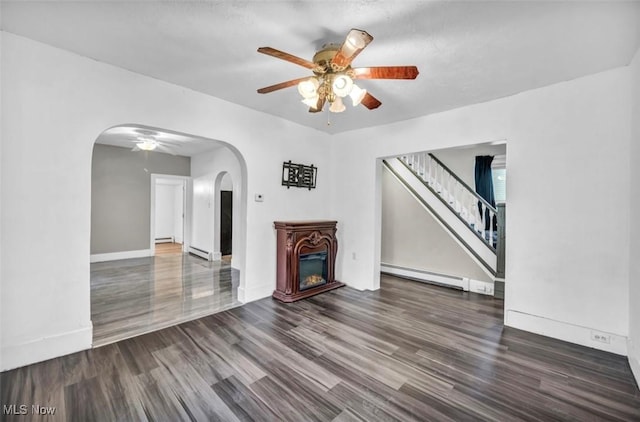 unfurnished living room featuring baseboard heating, ceiling fan, and dark hardwood / wood-style floors