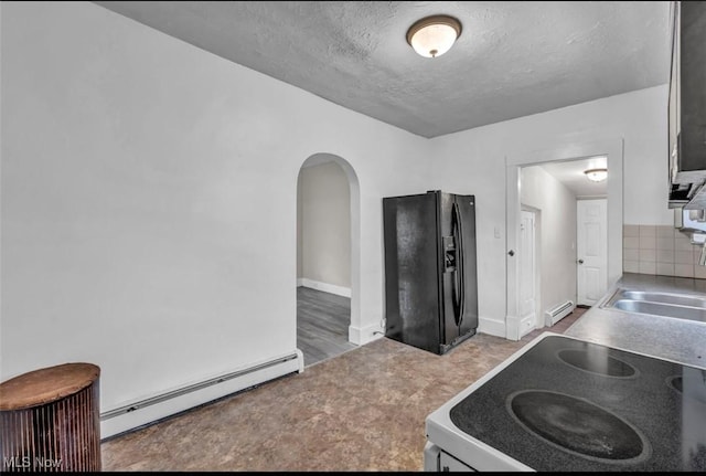 kitchen with black fridge, stove, a textured ceiling, and a baseboard heating unit