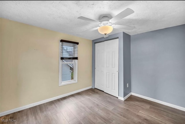 unfurnished bedroom featuring wood-type flooring, a textured ceiling, a closet, and ceiling fan