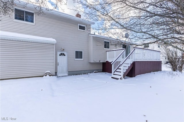 snow covered back of property with a wooden deck