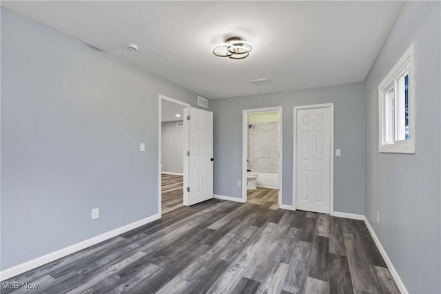 unfurnished bedroom featuring a closet, ensuite bathroom, and dark hardwood / wood-style flooring