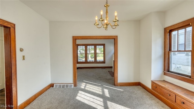 carpeted spare room featuring plenty of natural light and a notable chandelier