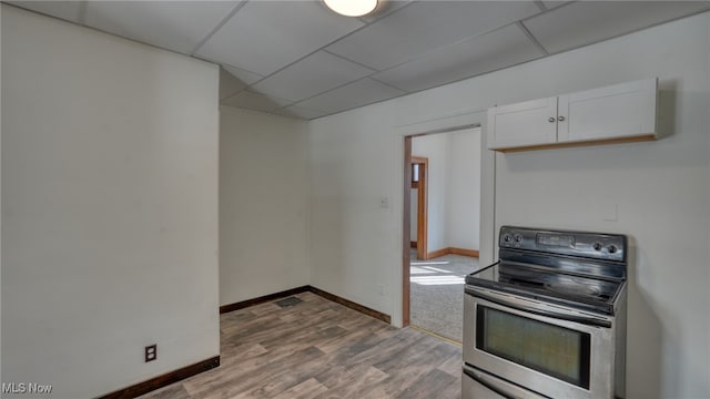 kitchen featuring stainless steel range with electric stovetop, a paneled ceiling, white cabinets, and light hardwood / wood-style flooring