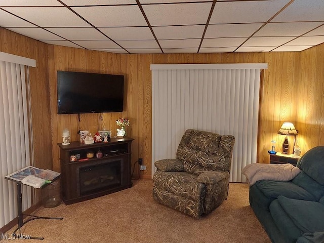 carpeted living room with a drop ceiling and wooden walls