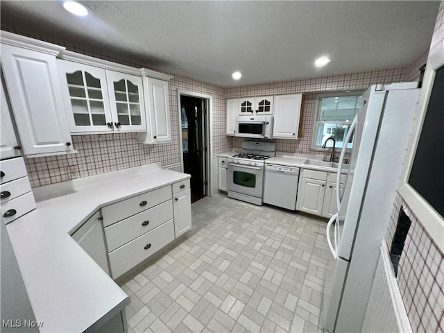 kitchen featuring tasteful backsplash, white cabinetry, sink, and white appliances