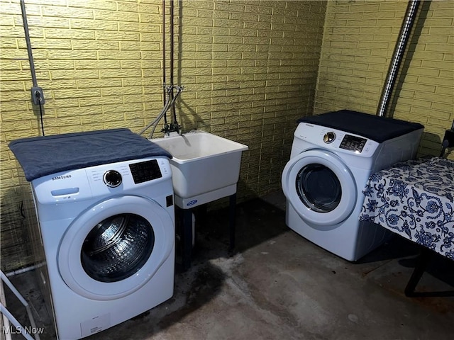 clothes washing area with sink, brick wall, and washing machine and clothes dryer