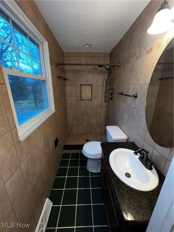 bathroom featuring tile patterned flooring, a tile shower, toilet, and tile walls