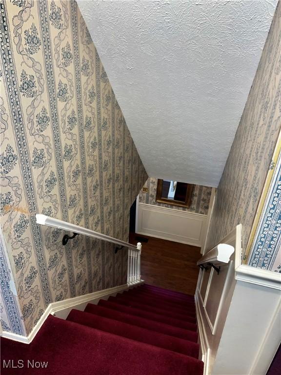 stairs with wood-type flooring, a textured ceiling, and vaulted ceiling