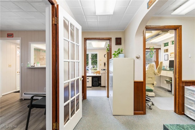 hallway with carpet, french doors, baseboard heating, and wooden walls