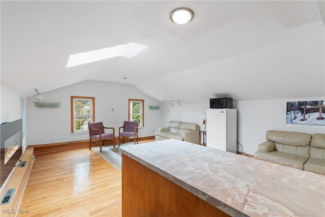 bedroom featuring light wood-type flooring, white fridge, and lofted ceiling with skylight