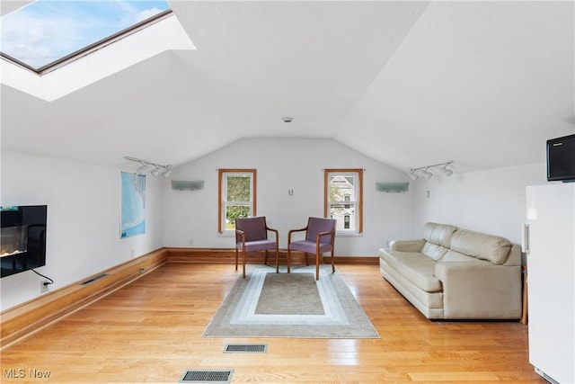 living room featuring vaulted ceiling with skylight, a wall unit AC, and light hardwood / wood-style flooring