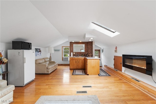 living room with lofted ceiling with skylight, a fireplace, and light hardwood / wood-style floors