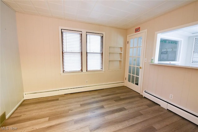 empty room featuring hardwood / wood-style floors, wooden walls, and a baseboard radiator