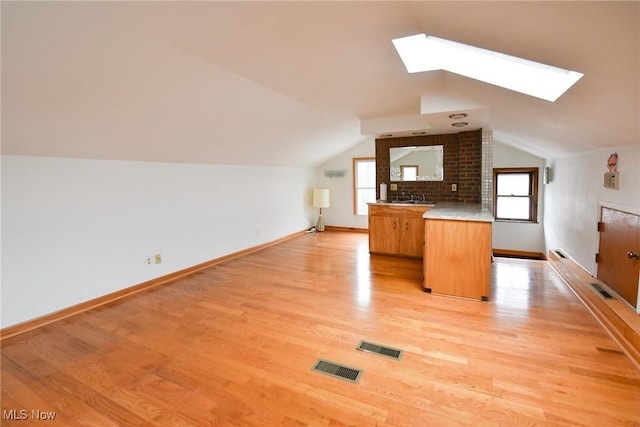 kitchen with kitchen peninsula, light wood-type flooring, sink, and lofted ceiling with skylight