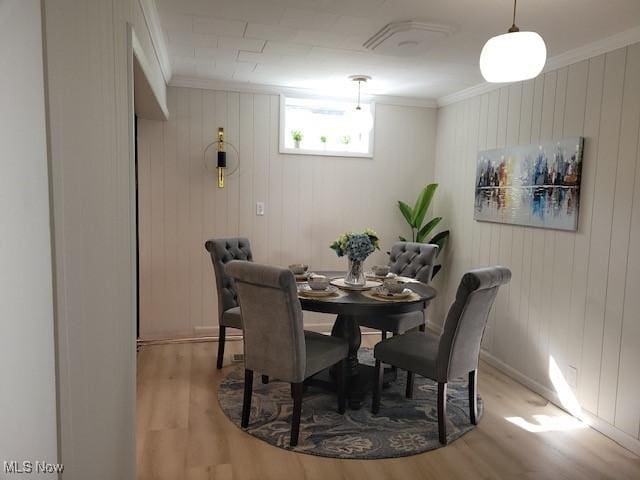 dining room with wood walls, light hardwood / wood-style floors, and crown molding