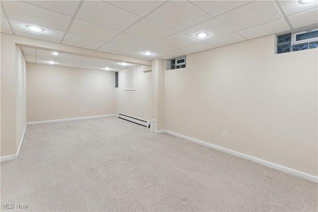 basement featuring a drop ceiling, light carpet, and a baseboard radiator