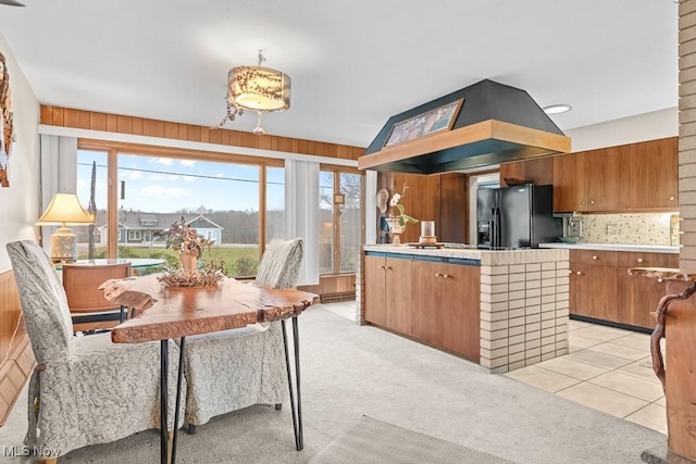 kitchen with black refrigerator with ice dispenser, wood walls, light colored carpet, a kitchen island, and custom exhaust hood