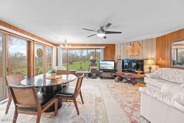 dining area featuring wood walls, plenty of natural light, and ceiling fan with notable chandelier