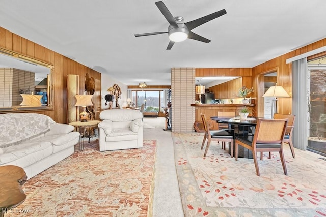 carpeted living room with ceiling fan and wood walls