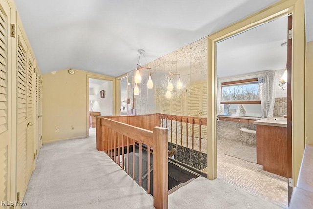 corridor featuring light carpet, vaulted ceiling, and an inviting chandelier