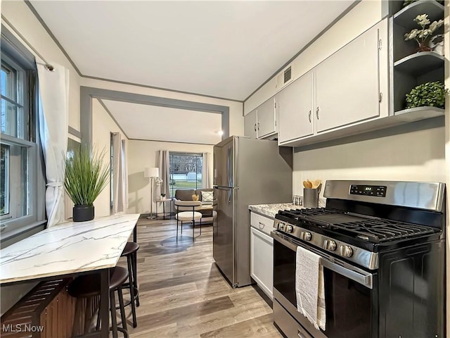 kitchen featuring white cabinets, a breakfast bar area, light stone countertops, light hardwood / wood-style floors, and stainless steel appliances