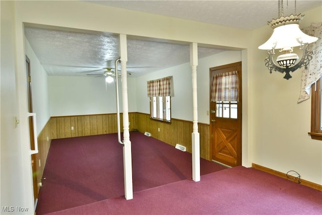 interior space featuring ceiling fan, a textured ceiling, and wooden walls