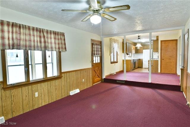 spare room with a textured ceiling, light colored carpet, ceiling fan, and wood walls