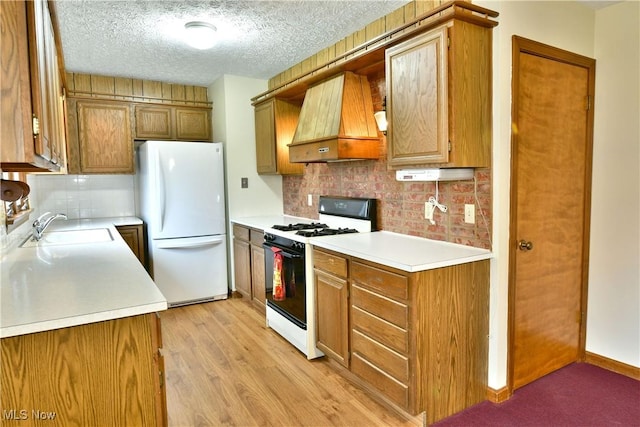 kitchen with custom exhaust hood, white appliances, sink, light hardwood / wood-style flooring, and a textured ceiling